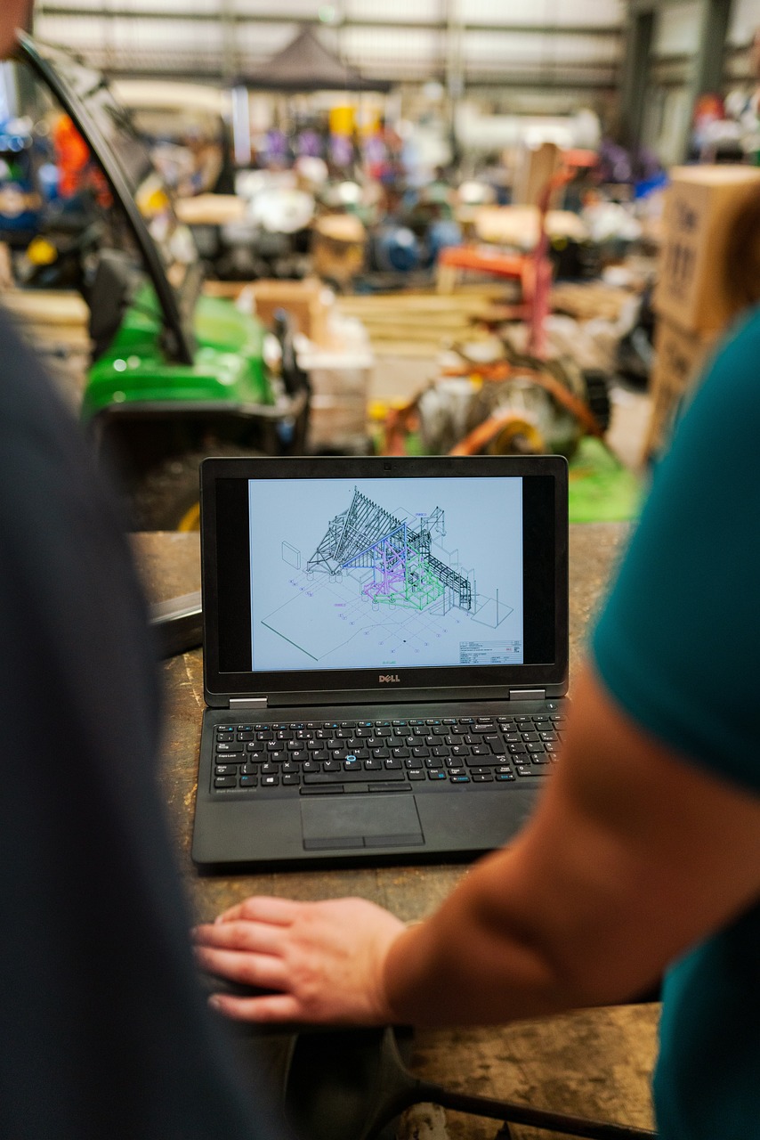 Inżynier analizujący rysunek techniczny na laptopie w hali produkcyjnej